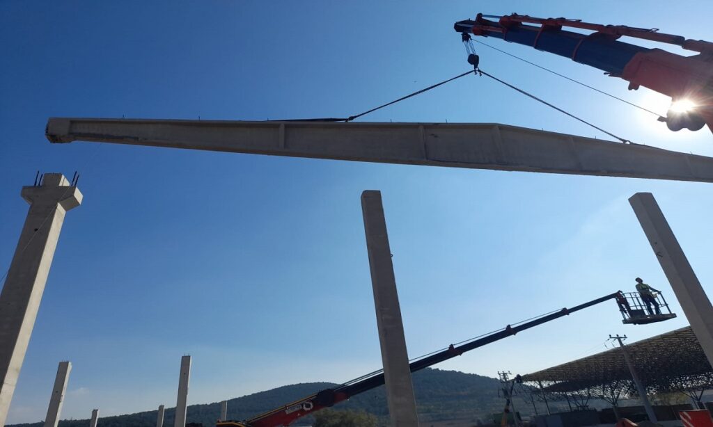 Vinçle prefabrik kolonların üzerine indirilen beton kiriş; sağda sepetli platformda montaj ekibi