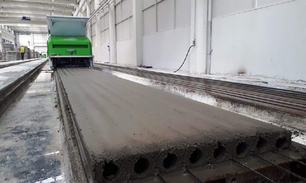 Üretim hattında dökülmüş boşluklu döşeme; arkada yeşil döküm makinesi