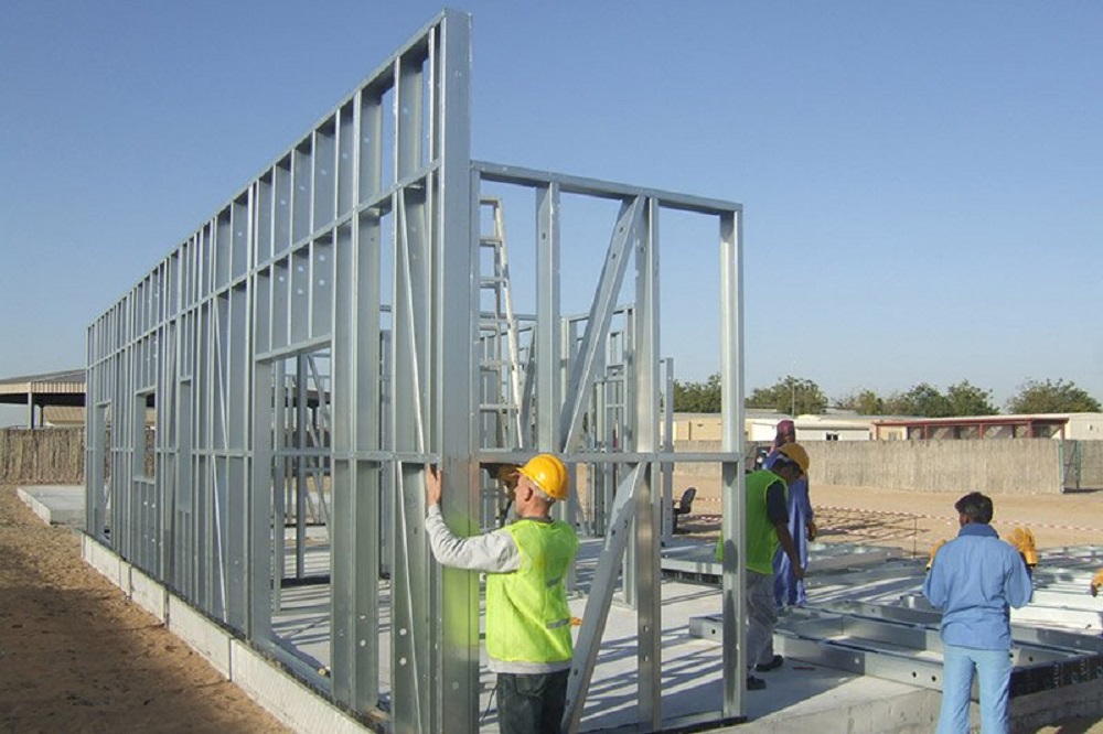 Sahada galvaniz hafif çelik duvar panelini dikey tutan baretli işçiler